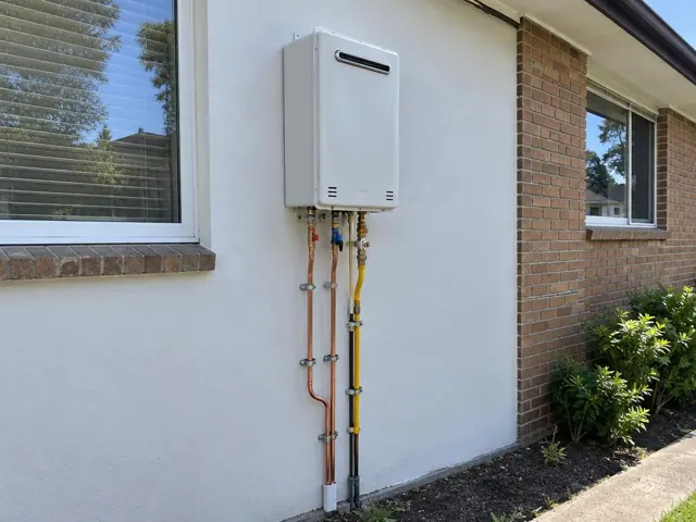 Outdoor gas hot water unit mounted on a rendered brick house wall with copper pipework in St Clair