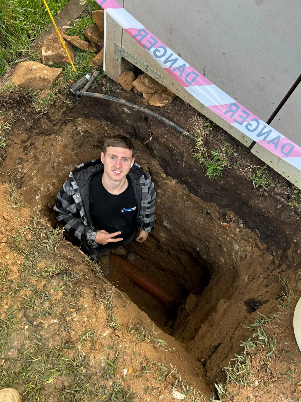 A plumber in a narrow dug pit tracing a hidden leak
