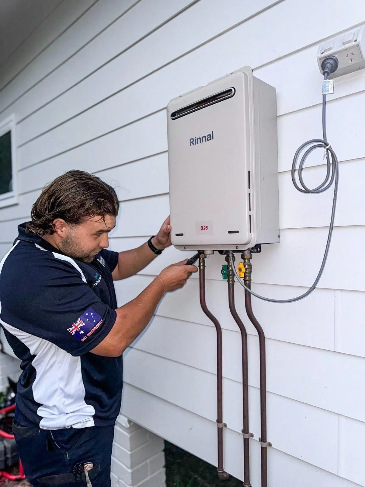 A plumber wiring a tankless hot water unit to an exterior wall